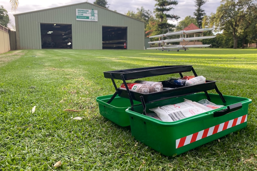 A green first aid kit sits in front of a green shed while sitting on green grass.