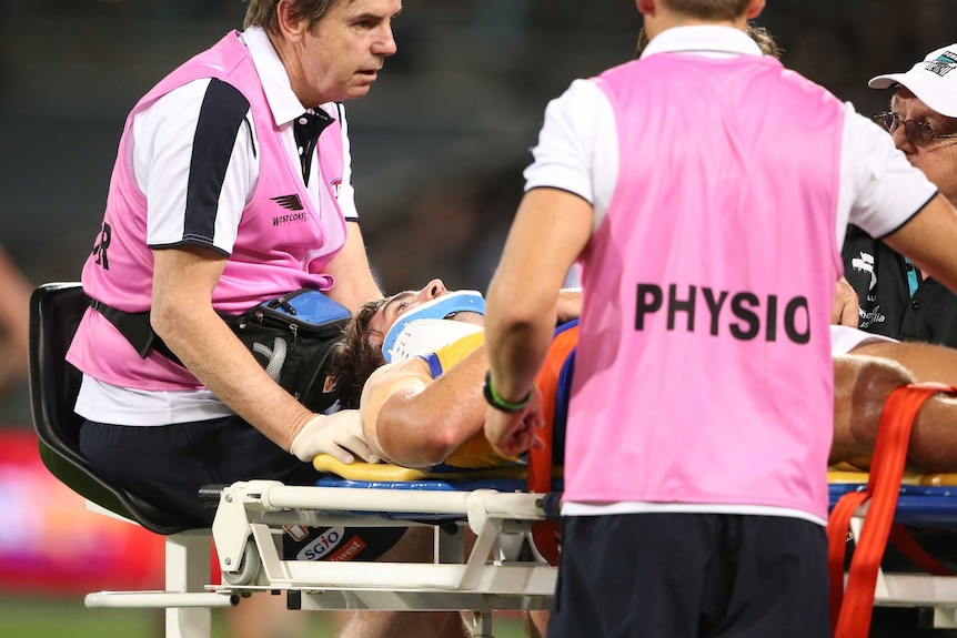 Andrew Gaff of the West Coast Eagles is stretchered off the field in a neck brace on a cart by two medicos in pink vests.