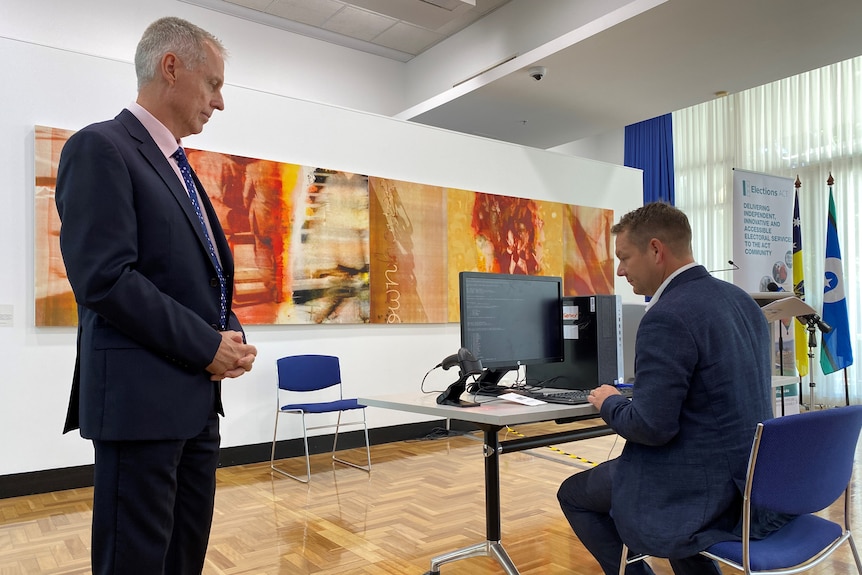 Two men watch as one of them uses a computer.