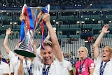Ellie Carpenter, with a brace on her left leg, lifts the Champions League trophy in front of her Lyon teammates.