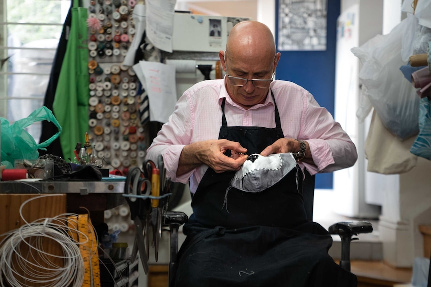 a man stitching a black pattern onto a cloth inside a tailor shop