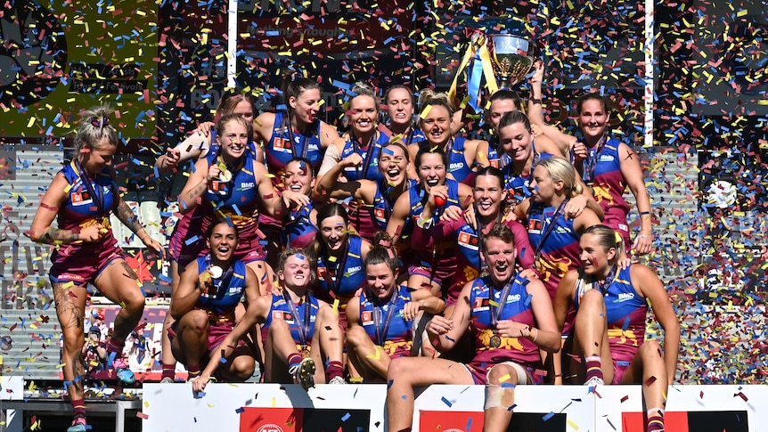 Brisbane Lions players celebrate winning the AFLW grand final, holding the trophy as confetti rains down