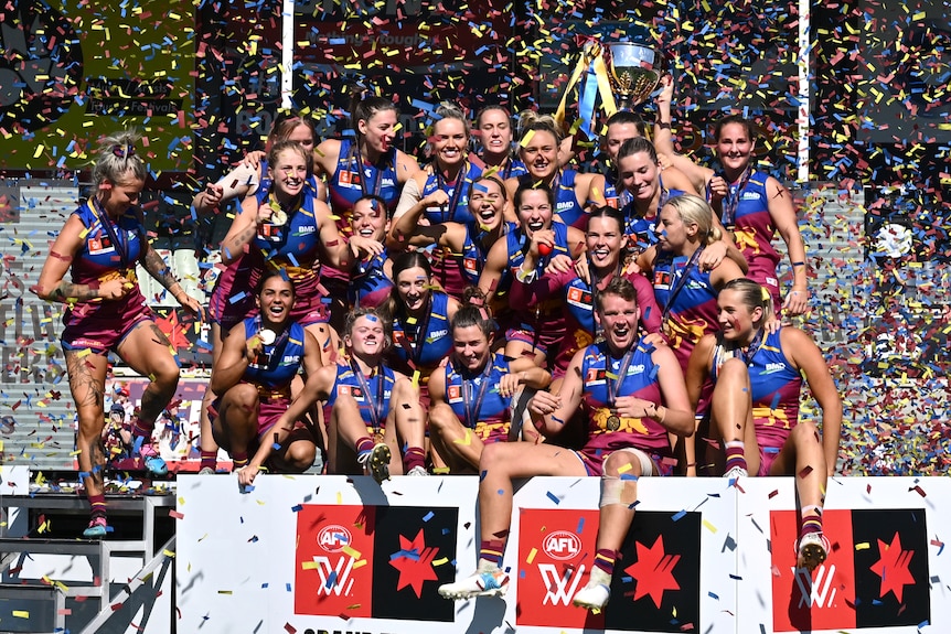 Brisbane Lions players celebrate winning the AFLW grand final, holding the trophy as confetti rains down