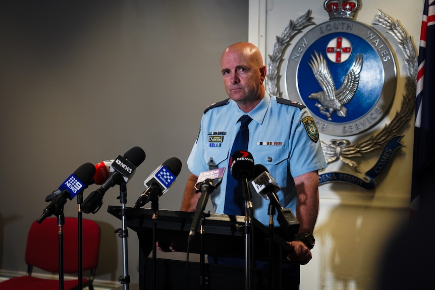 NSW Police Superintendent Martin Fileman addressing the media with microphones in front of him, crest behind him