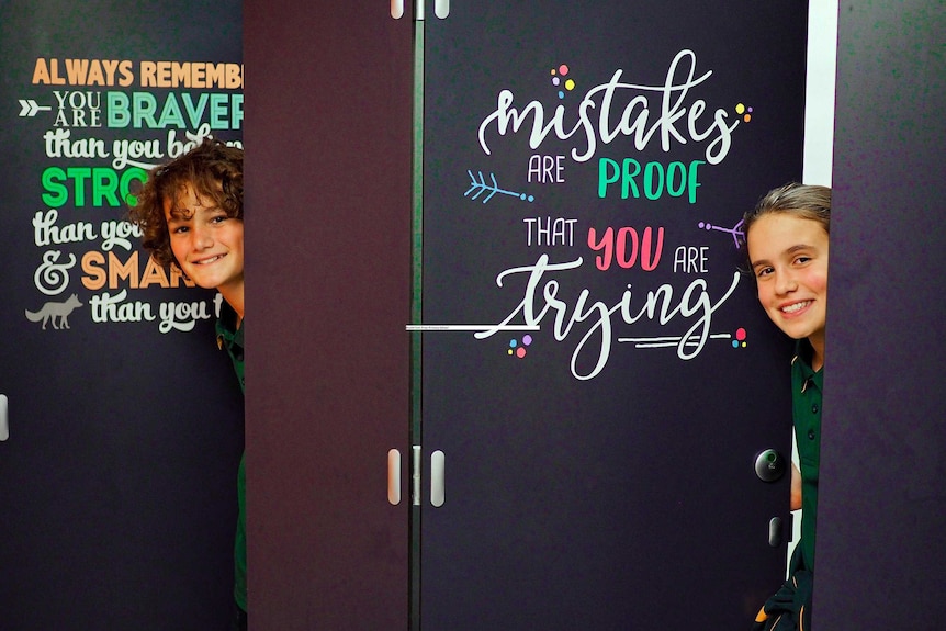 A boy and a girl poke their heads around doors with positive messages written on them.