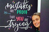 A boy and a girl poke their heads around doors with positive messages written on them.