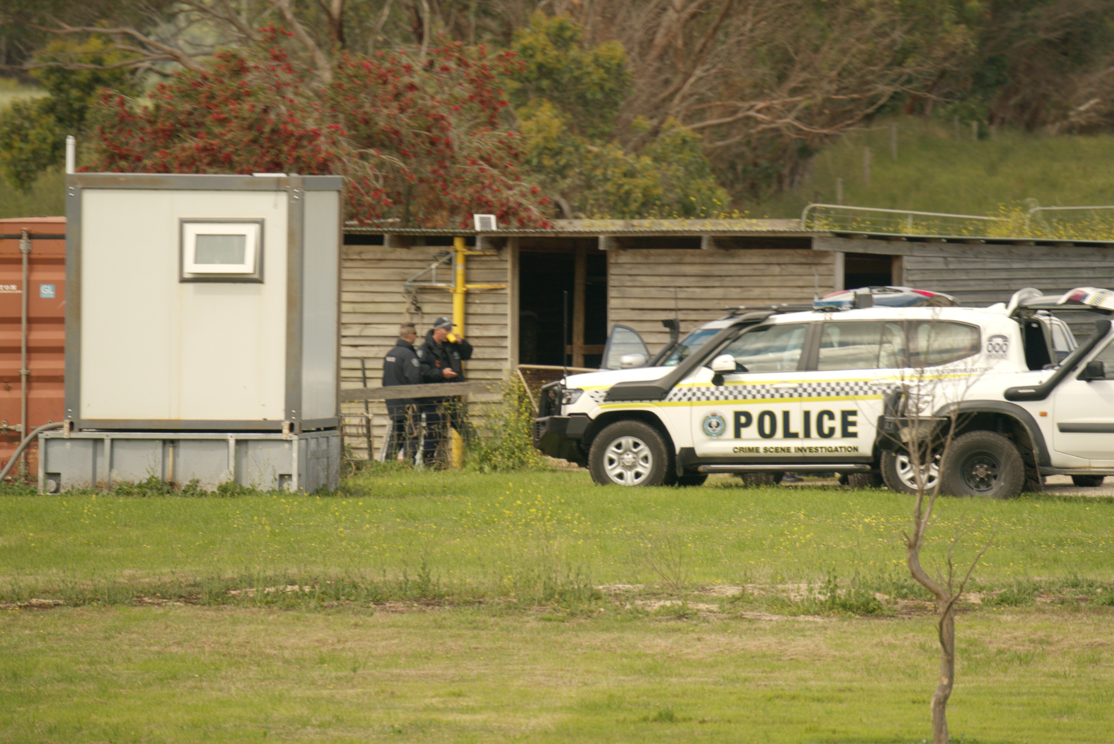 Dos agentes de policía junto a un vehículo policial de cuatro ruedas y un refugio de madera en la hierba verde