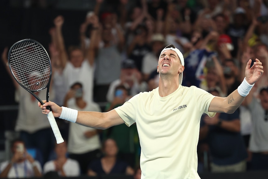 Male tennis player, eyes closed, looking upward, arms raised in triumph.