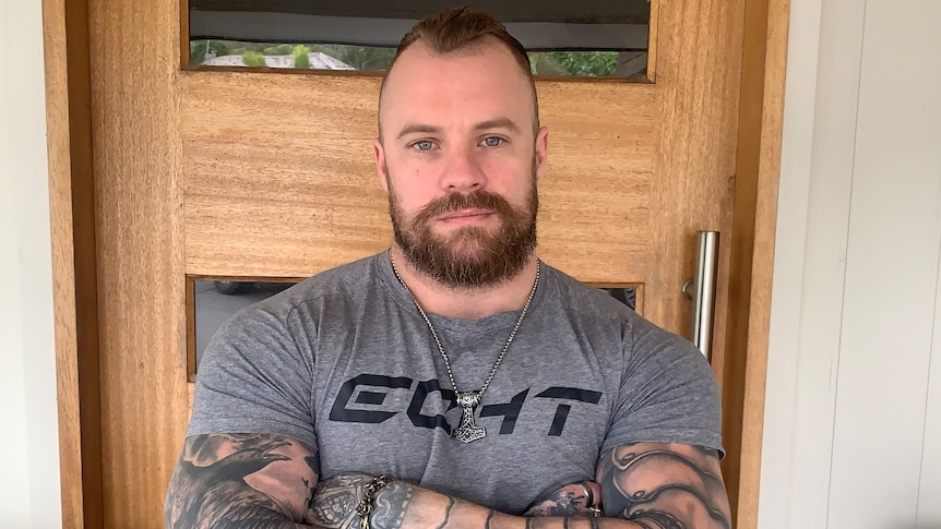 Daniel Lees wears a grey t-shirt in front of a home's front door.