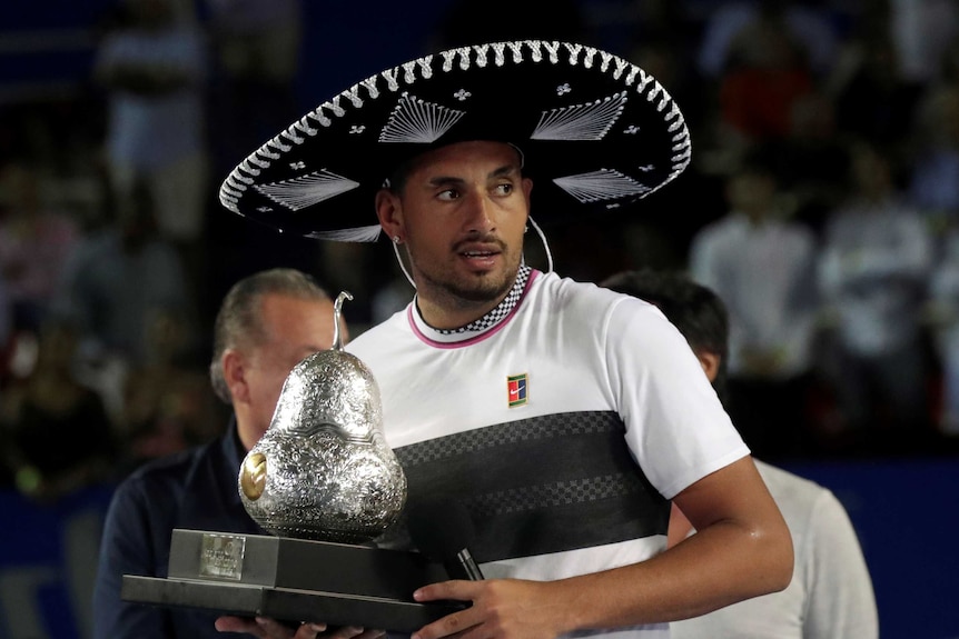 Nick Kyrgios wears a sombrero and holds a trophy and a microphone after winning Acapulco ATP Tour event.
