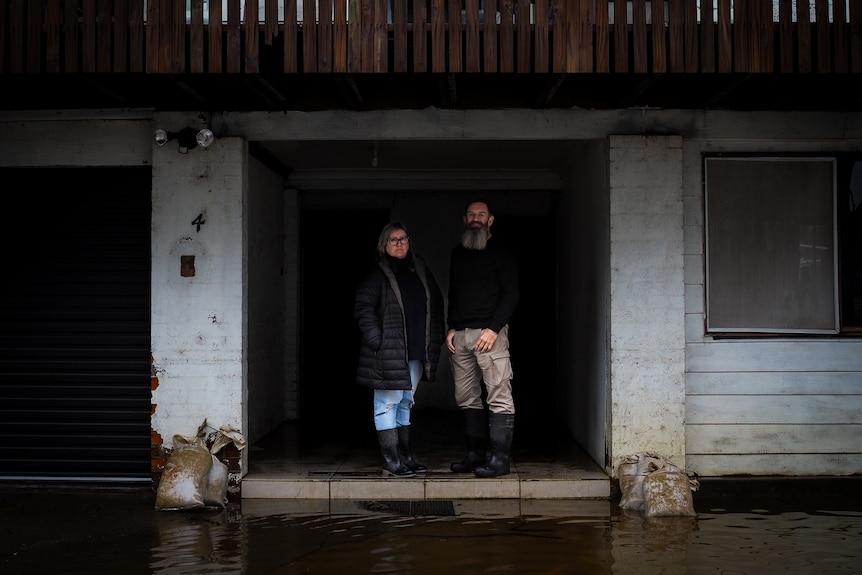 DeAnn and Brant Gilliver stand on their doorstep with floodwaters below them.