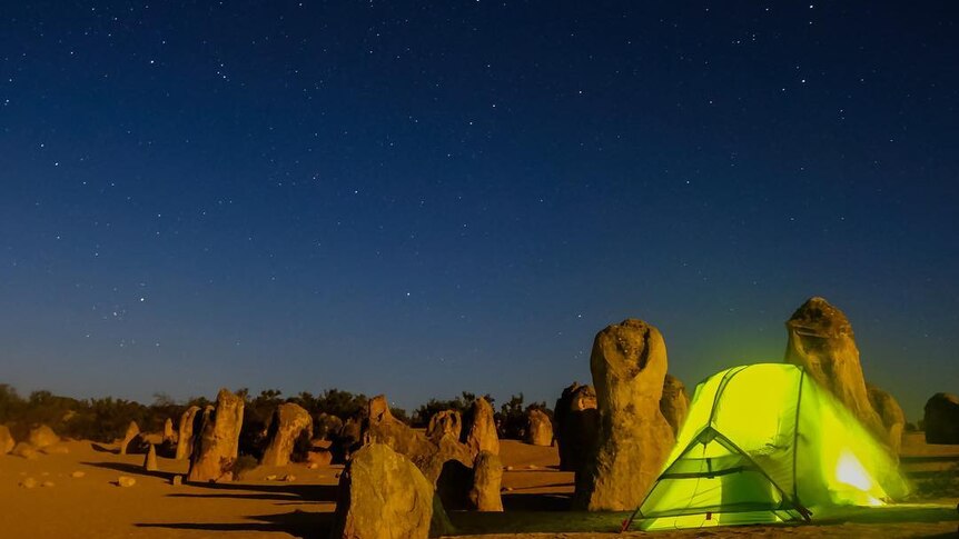 A glowing tent is pitched under the stars, surrounded by the rock mounds of the Pinnacles National Park.