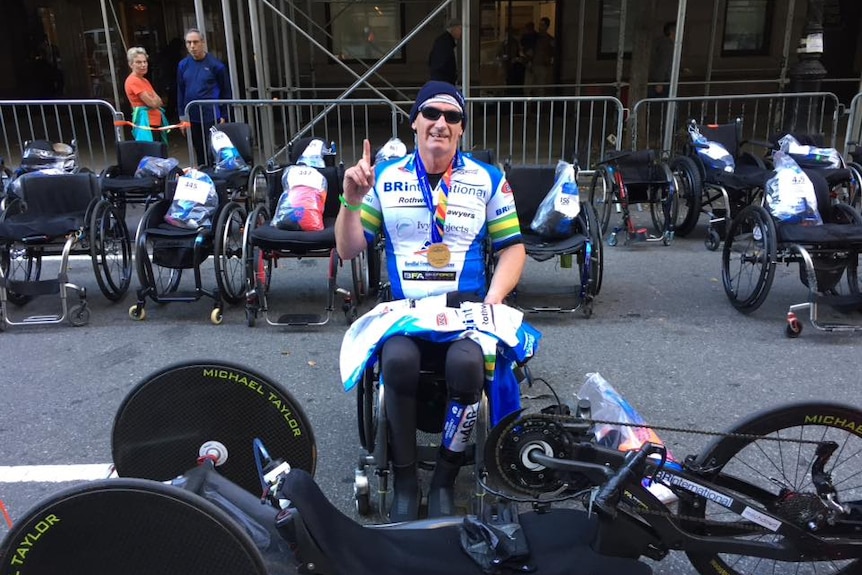 Michael Taylor in his wheelchair sitting behind his hand-cycle.