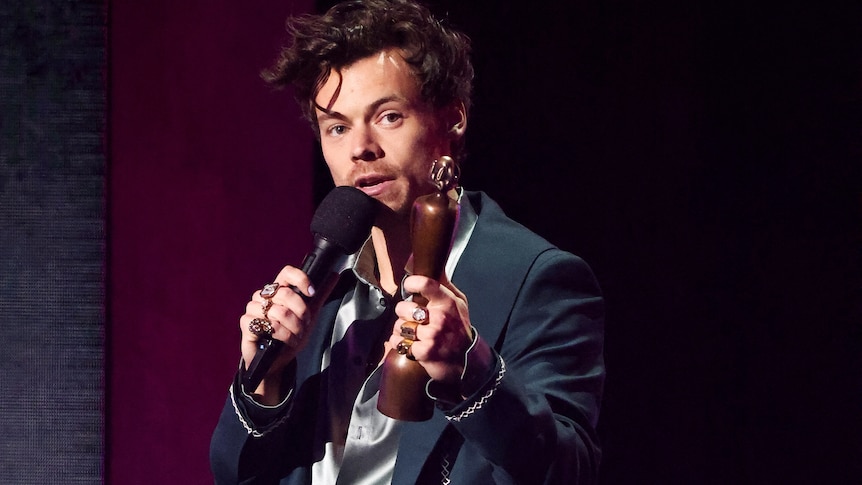 Harry Styles holds up a Brit Award and speaks into the microphone at the 2023 awards ceremony