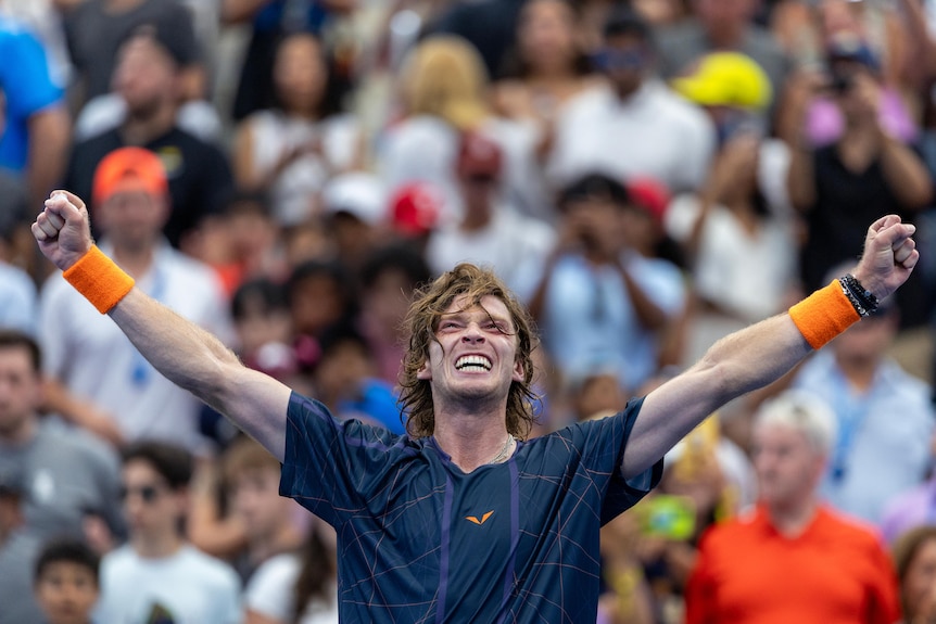 Andrey Rublev extends both arms, clenches his fists and smiles after winning a US Open tennis match.