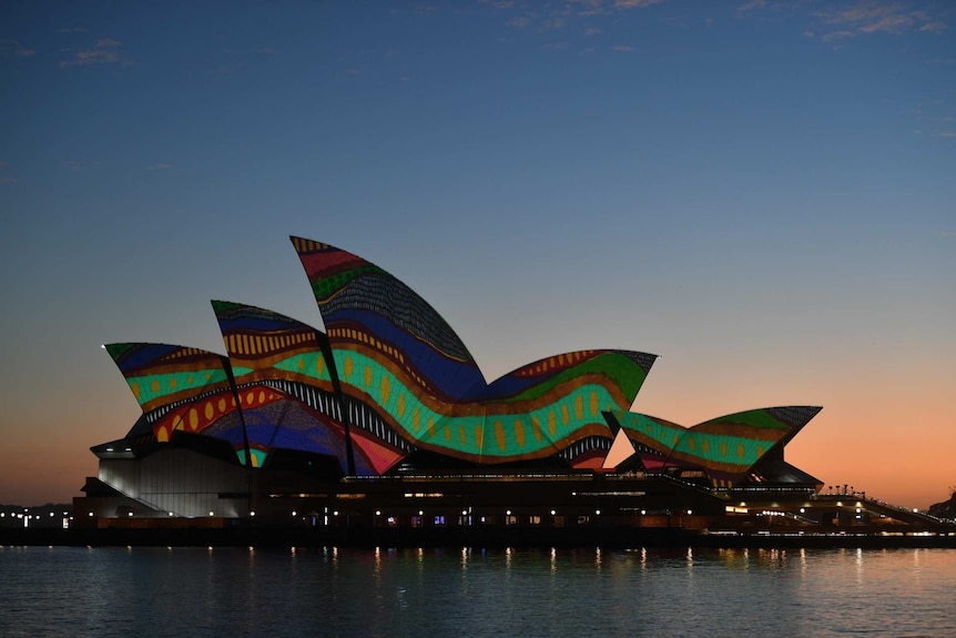 The sails of the Sydney Opera House are lit up at dawn with an Indigenous artwork