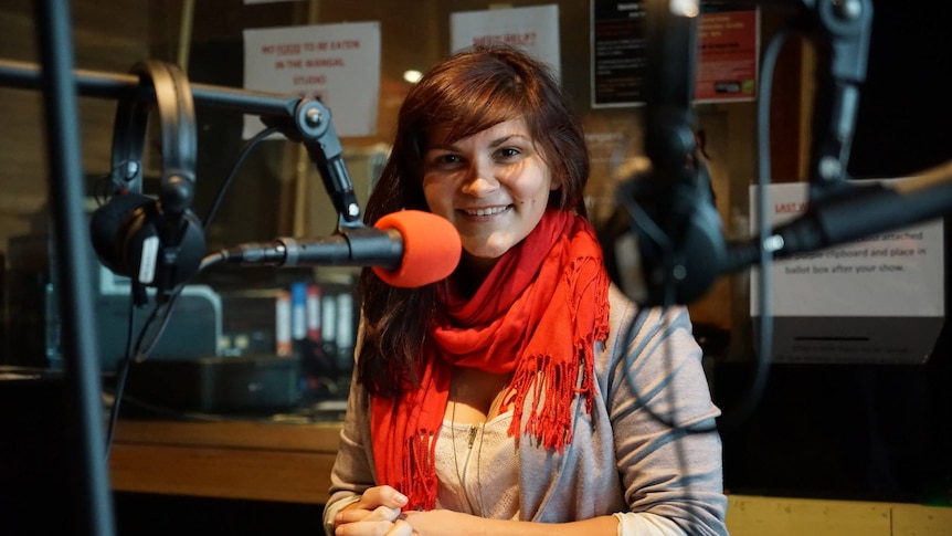 Zoe wearing red scarf and smiling in behind a microphone