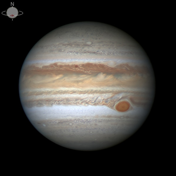 A photo of the planet Jupiter, there are rings in various shades of brown. To the right there is a big red spot.