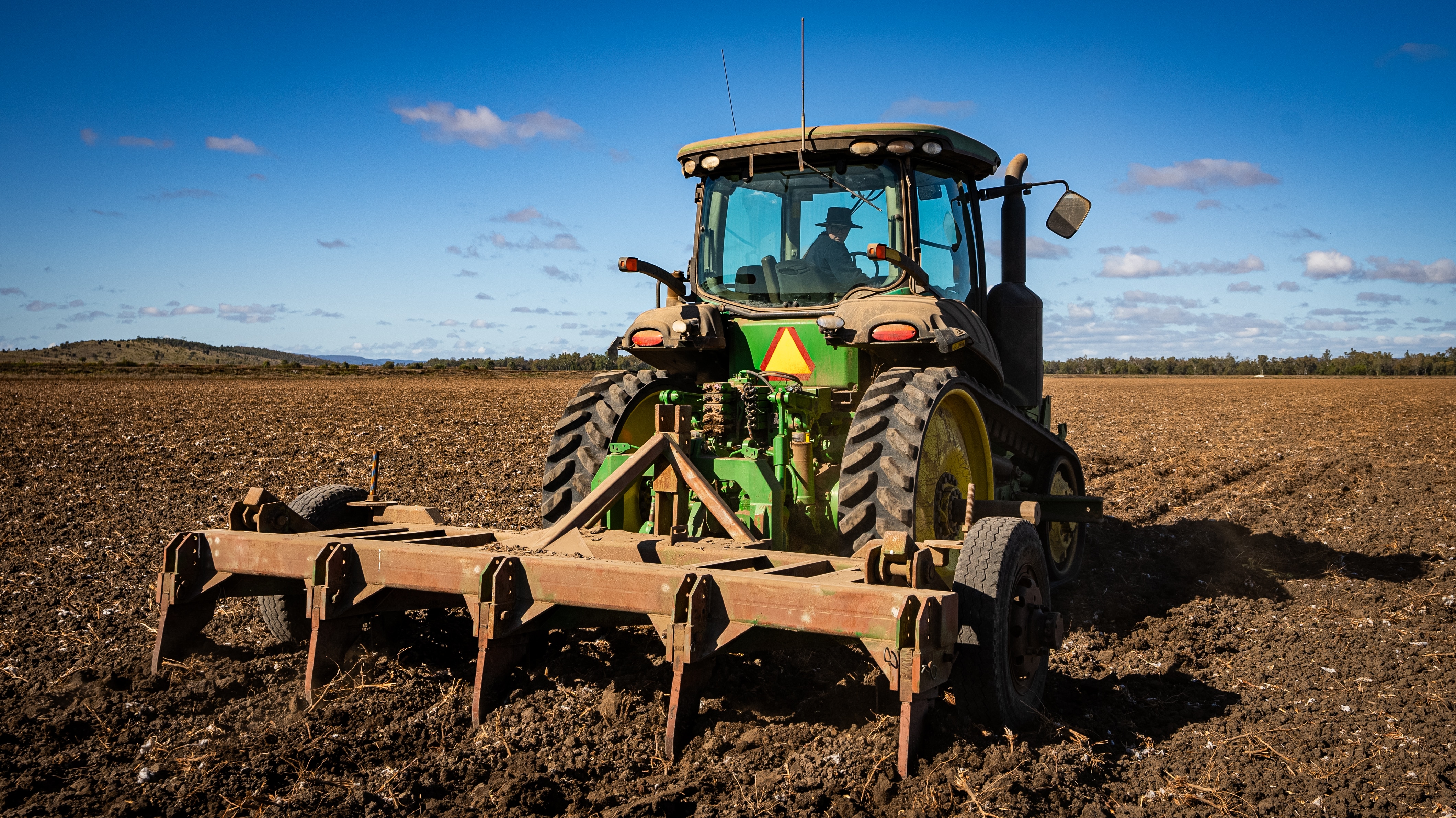 A tractor drives over dirt property, with a women inside driving it.