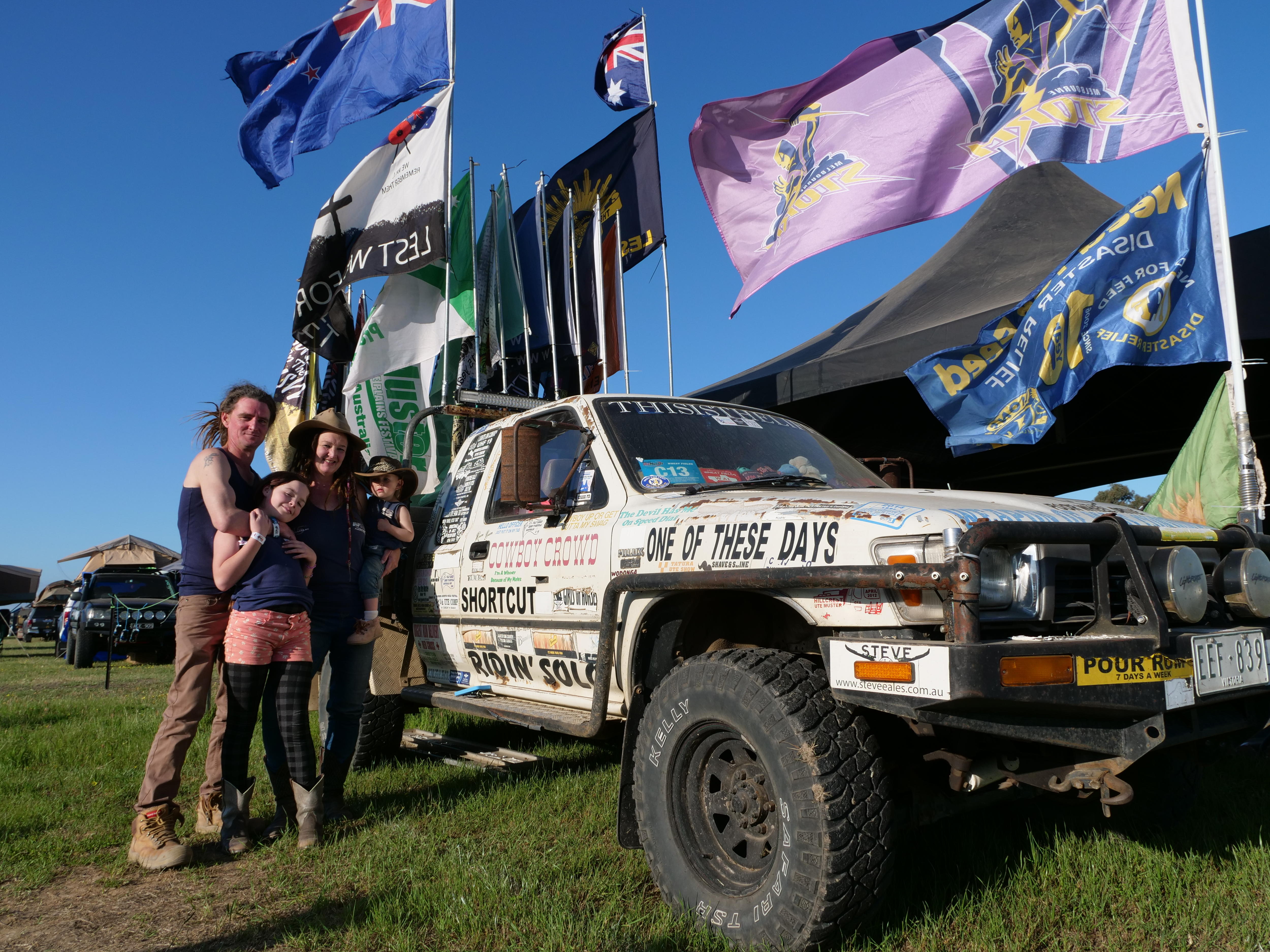 A family stands next to a ute adorned with flags and stickers.