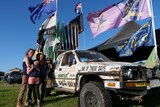 A family stands next to a ute adorned with flags and stickers.