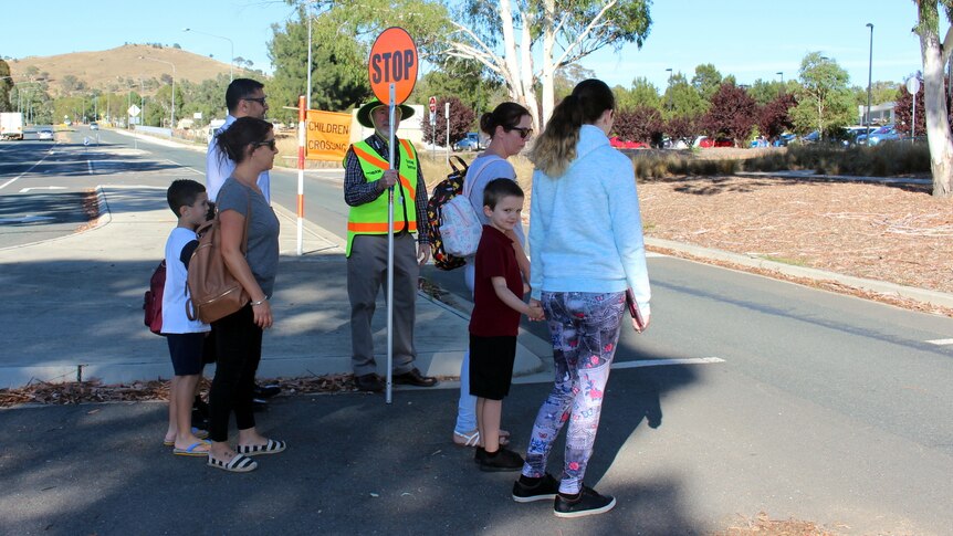 Families cross over a road crossing outside a school.
