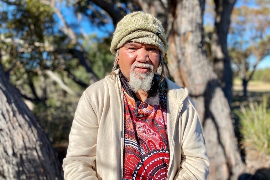 Aboriginal man standing in the bush wearing bright red shirt and green beanie smiling with the sun on his face