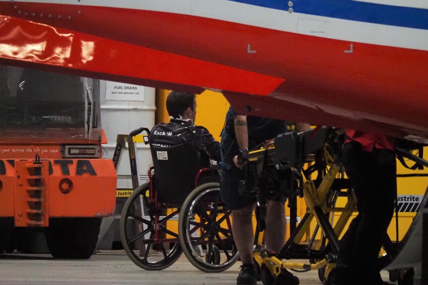 The back of a man's head who is sitting in a wheel chair near an ambulance and paramedic.