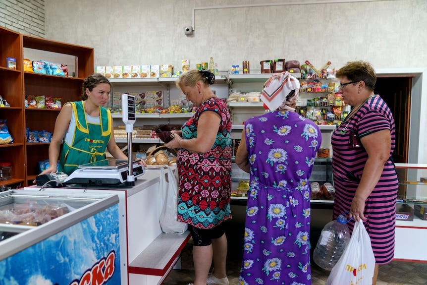 A woman at a register with three people in line at a shop