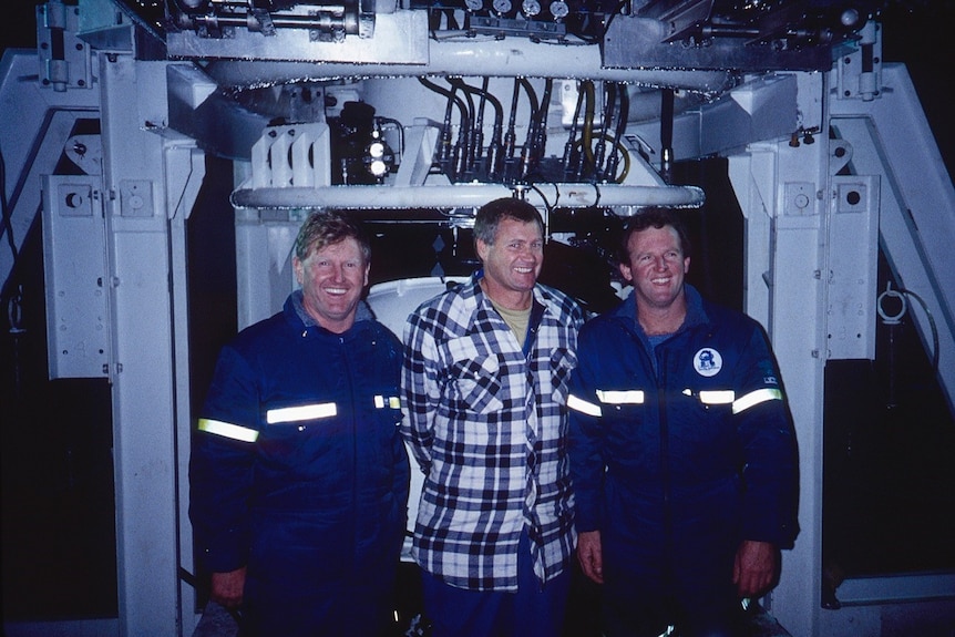 Three men smile at the camera in a submarine