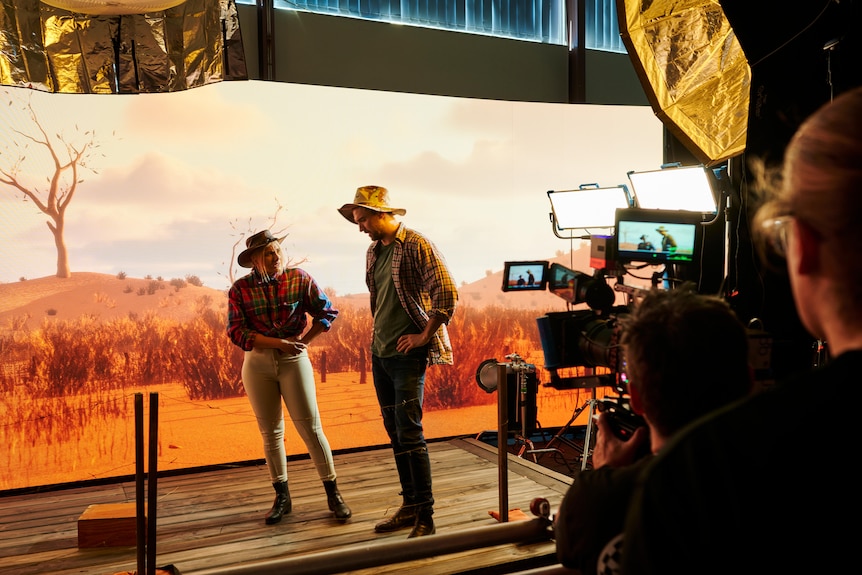 A cameraman in the foreground filming two people seated on stage