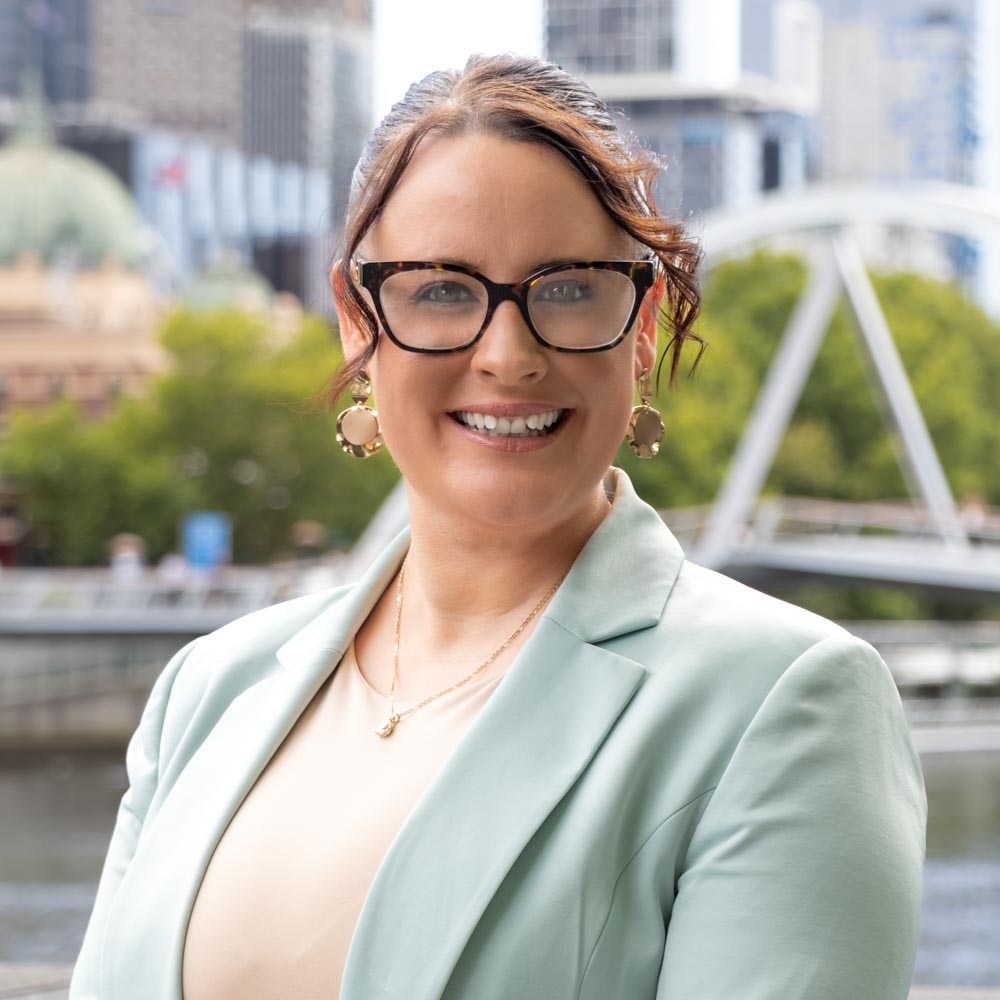 A woman with brown curly hair wearing a suit and a pair of glasses smiling at the camera.