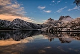 Cradle mountain under light snow at sunrise with Dove Lake showing it reflected in the foreground.