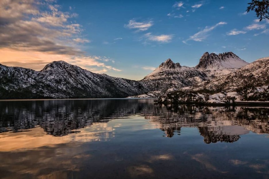 Cradle mountain under light snow at sunrise with Dove Lake showing it reflected in the foreground.