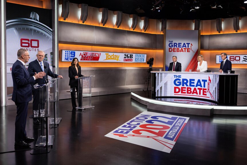 The studio set up for the debate. Leaders stand on the left, three journos sit behind a curved desk on the right