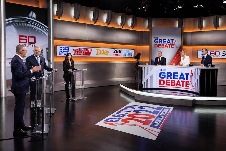 The studio set up for the debate. Leaders stand on the left, three journos sit behind a curved desk on the right