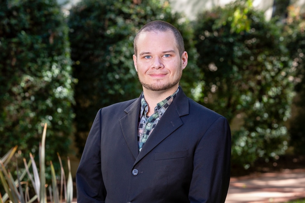 A man wearing a suit looks at the camera and smiles with a closed mouth.