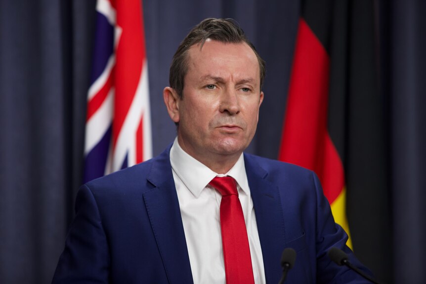 Mr McGowan looks resolutely forward, standing between the Aboriginal flag and Australian flag.