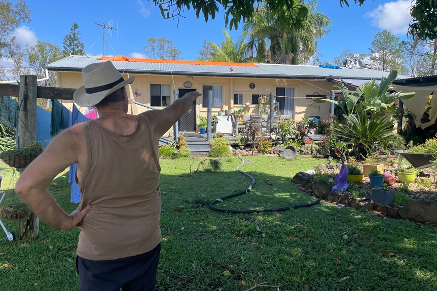 Geoff standing in his backyard pointing to tarps put on his roof 