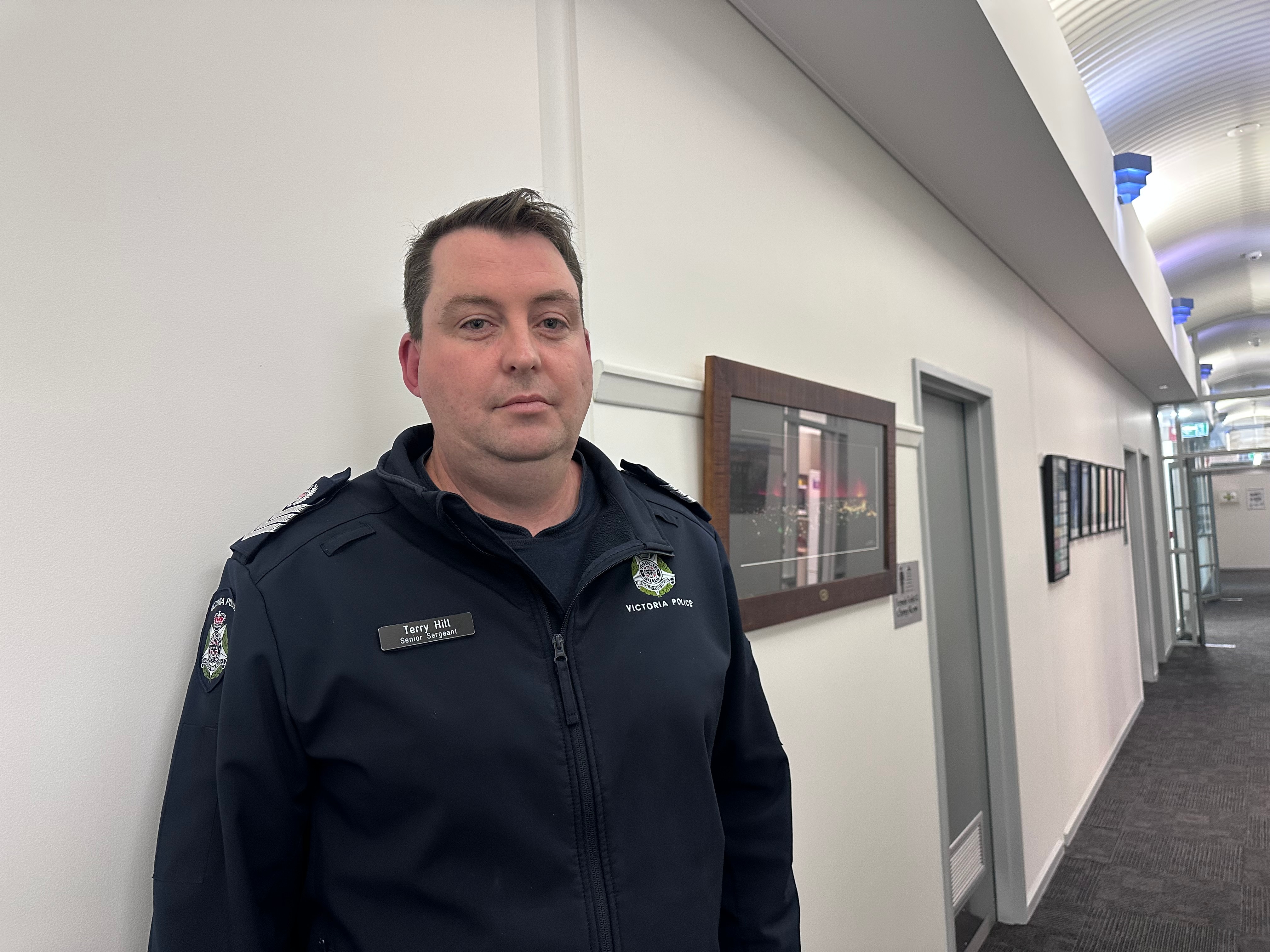 Police officer man looking seriously into camera, in hall way within the Stawell police building, frames on walls.