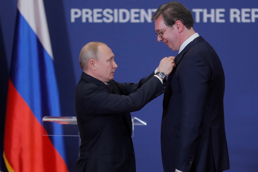 Mr Putin is reaching up and attach the order to Mr Vucic's jacket. 