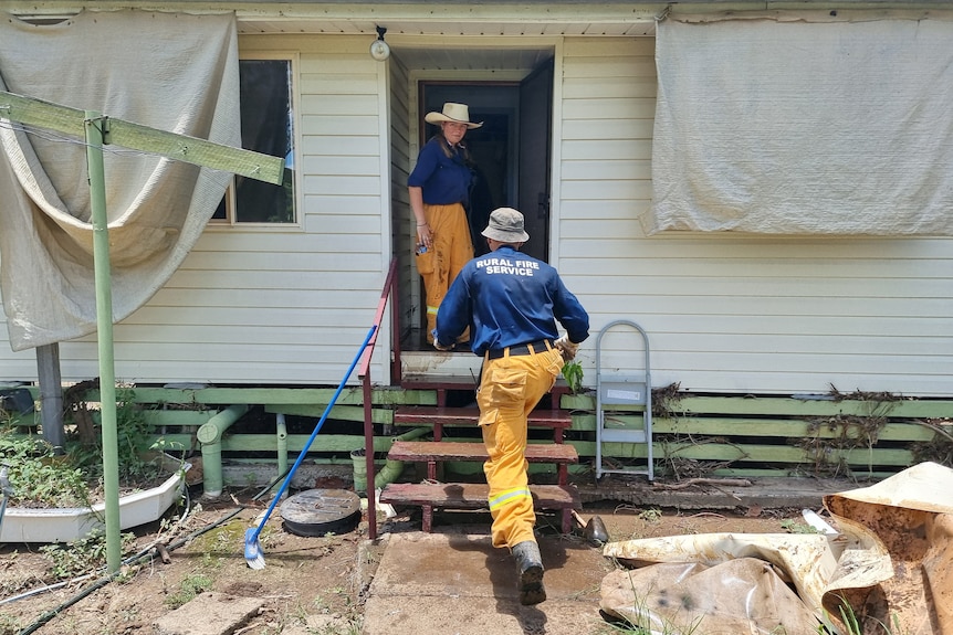 Rural fire brigade volunteers walk into a flood damaged house