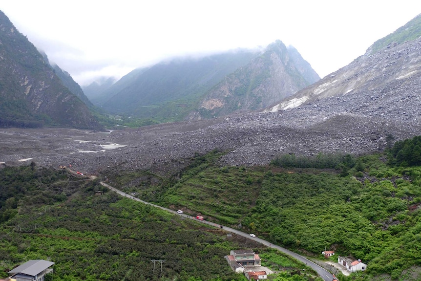 Cars and people line a road to Xinmo in this photo taken at a distance. You can see the entire village has been buried by rocks.