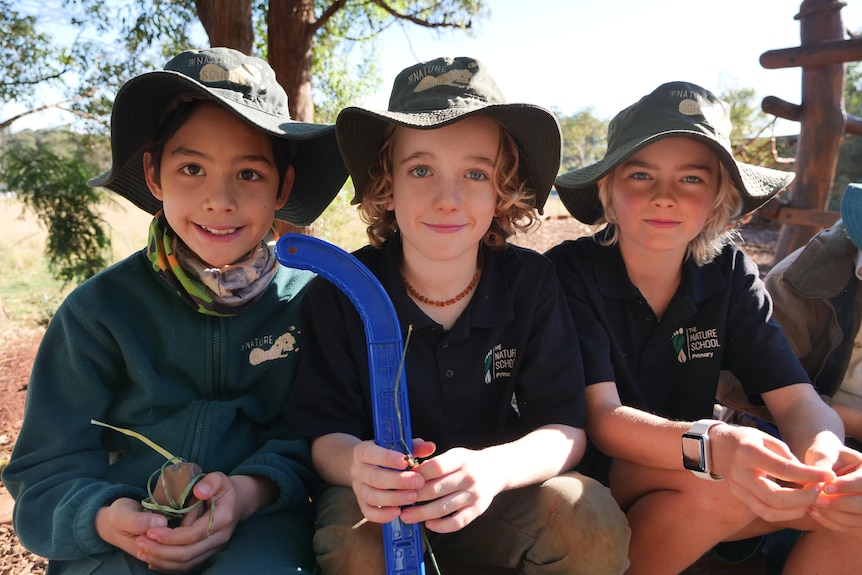 Close-up shot of three Year 3/4 boys seated and holding different items as they sit around the school's fire pit