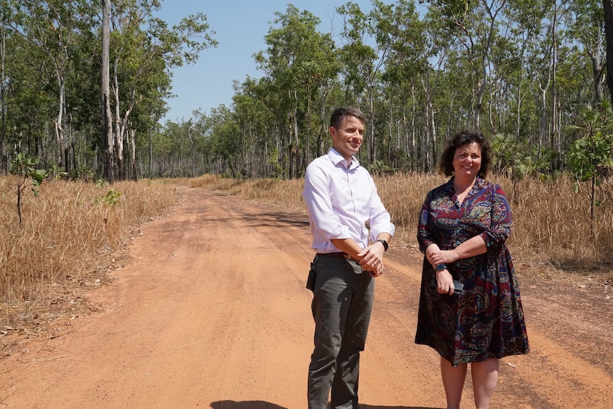 A man and a woman stand in a dirt road surround by scrub