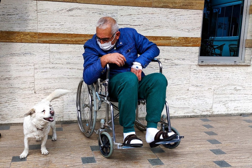 Cemal Senturk (right) wearing a blue jacket and green pants looks down at his dog Boncuk