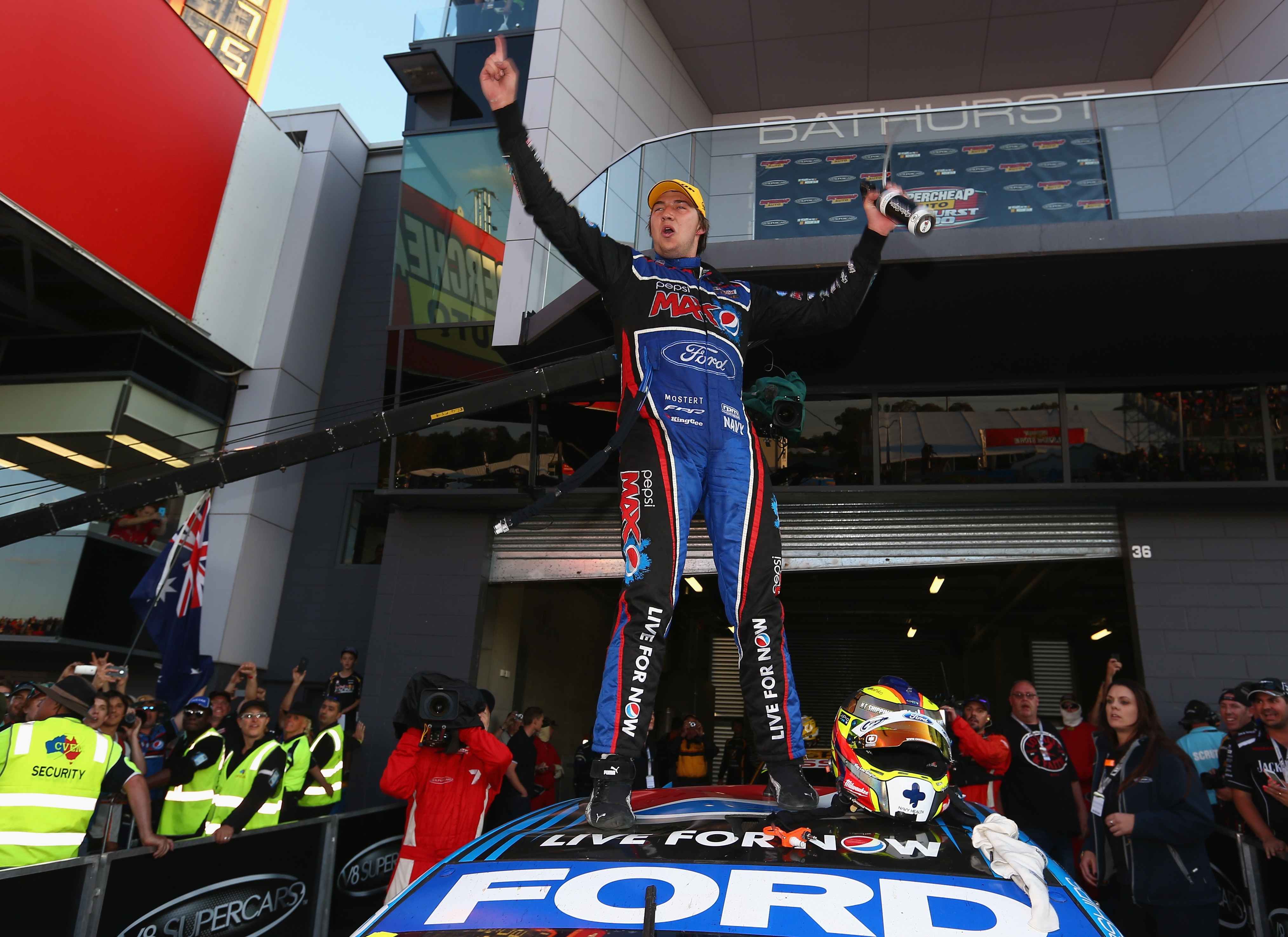A Ford racing driver strikes a pose standing triumphant on the roof of his car after a big win.  