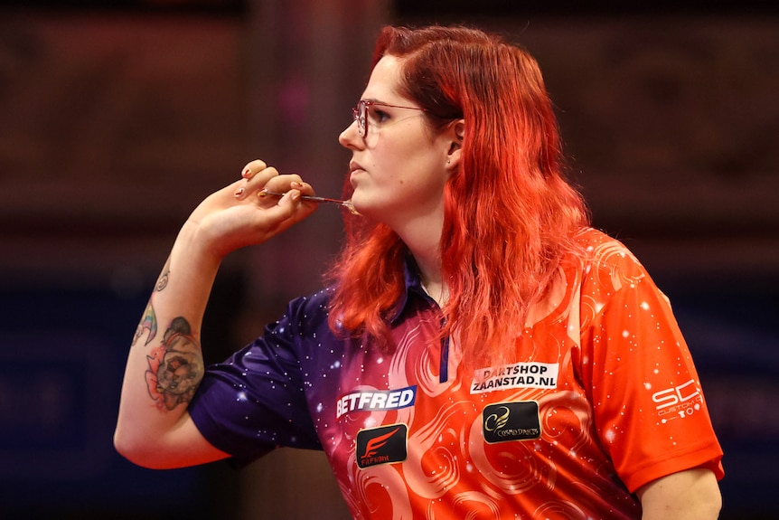 A woman is pictured from the side, she is about to throw a dart.