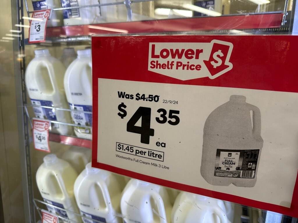 Milk bottles in a supermarket fridge with a red &#x27;Lower Shelf Price&#x27; sign in the window