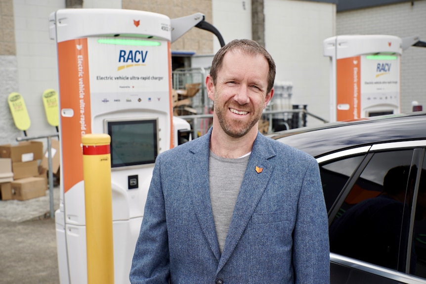 Martin Andrews wearing a grey suit and standing in front of an electric car charging station.